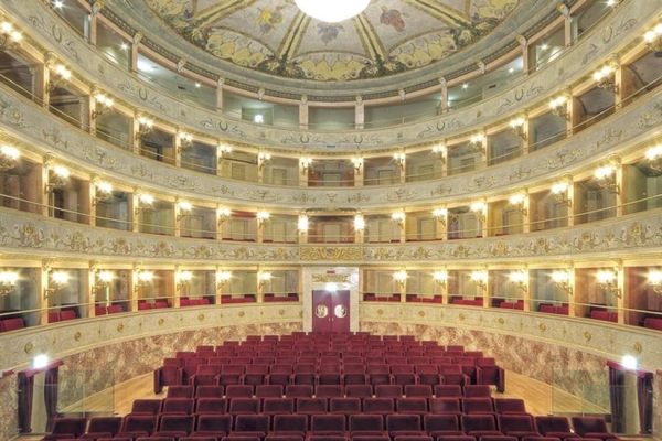 Interno di un teatro storico con balconate e poltrone rosse.